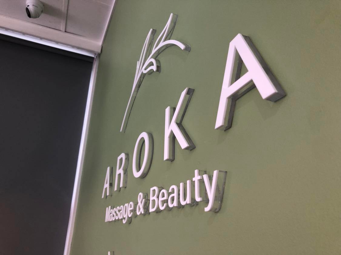 aroka massage and beauty white acrylic signage adhered to a sage green wall