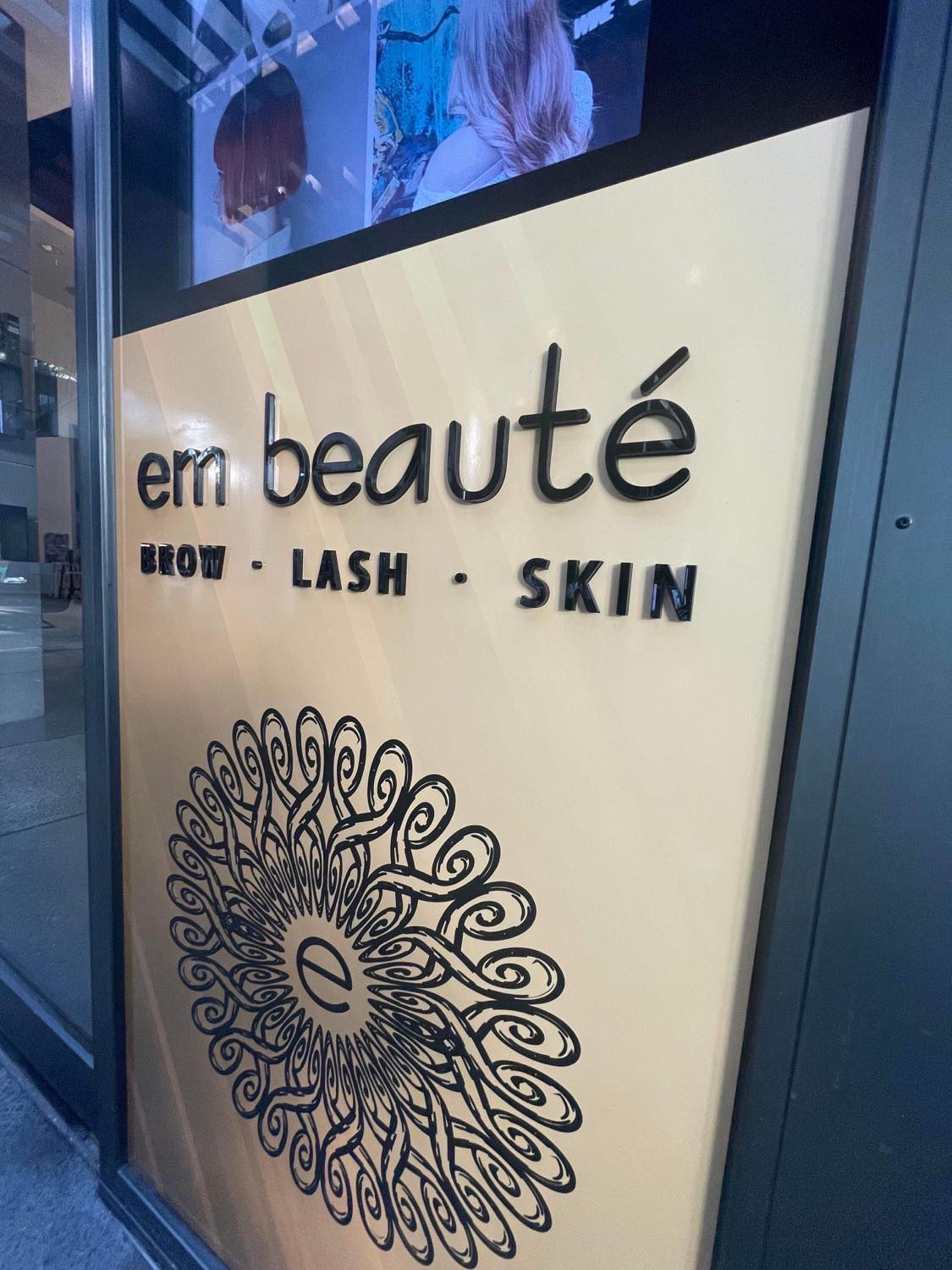 embeaute black  gloss acrylic signage adhered to a vinyl poster sign on wall of salon
